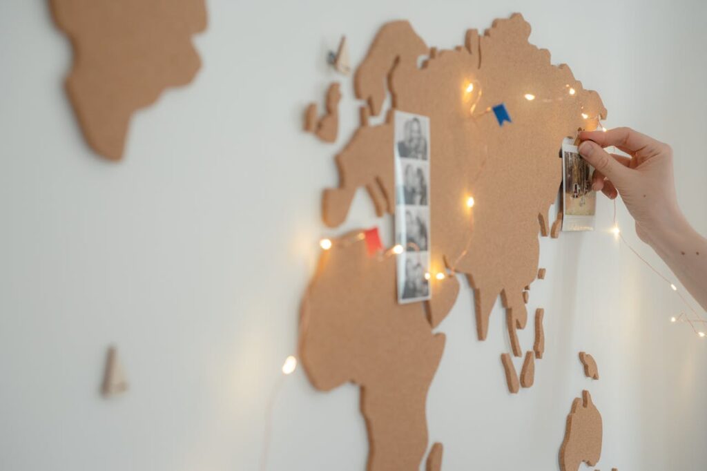 pexels-photo-7634437 Hand placing photo on cork world map adorned with fairy lights, ideal for travel decor inspiration.